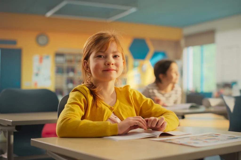 Young girl sitting at her desk in elementary school. Elementary school presents unique challenges for kids with mitochondrial diseases and their parents.