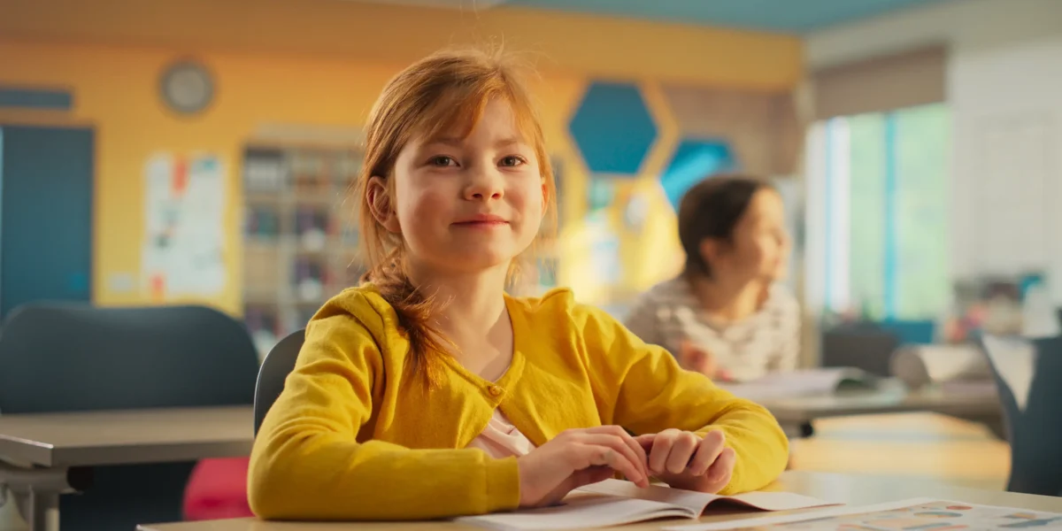 Young girl sitting at her desk in elementary school. Elementary school presents unique challenges for kids with mitochondrial diseases and their parents.